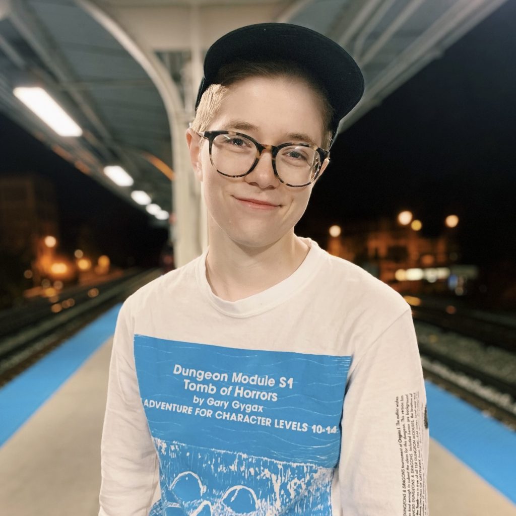 A photo of M. R. Robinson, a white woman with short hair, wearing a baseball cap and a Dungeons & Dragons t-shirt.